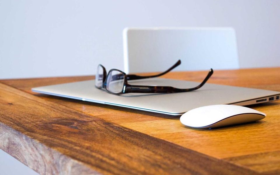 A desk with a laptop, glasses and notes